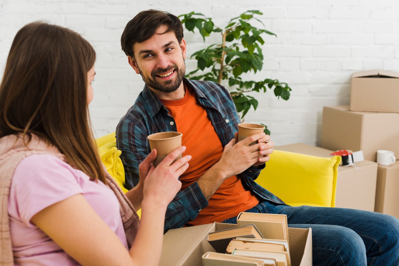 Two People Sitting With Coffee Cups, Surrounded By Moving Boxes In A Room