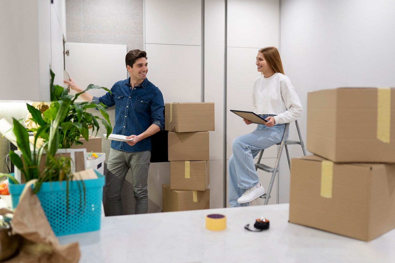 Two People With Cardboard Boxes In A Modern Kitchen, Possibly Moving In