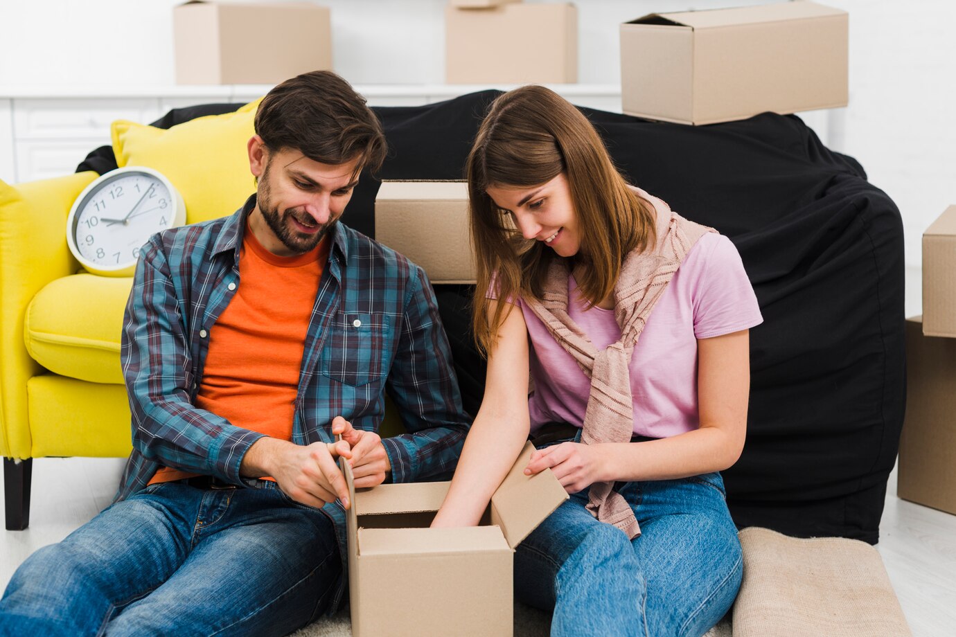 Two People Sitting On The Floor, Surrounded By Cardboard Boxes, Presumably Moving