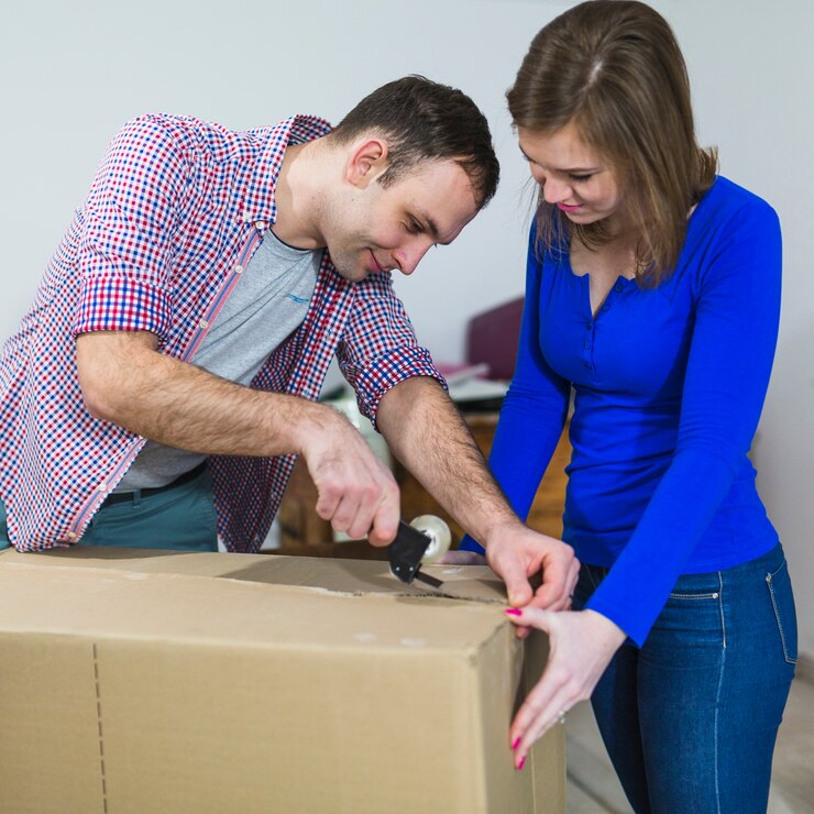 Two People Taping Up A Cardboard Box Together